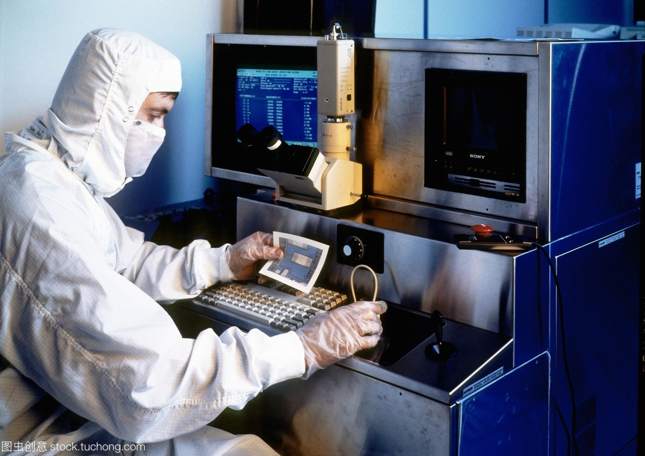 模型發布。硅晶片檢查。一名技術人員拿著一張硅片的部分照片,同時對其微電路進行檢查。他坐在顯微鏡下觀察晶圓的放大。這是一個&ldquo;干凈的房間&rdquo;,技術人員穿著一套身衣,兜帽和面罩。在所有過程涉及人工微電路的制作和測試技術人員穿防護服和手套空氣潔凈室的過濾。即使是最小的塵埃微粒也可能破壞其中的一個微電路。